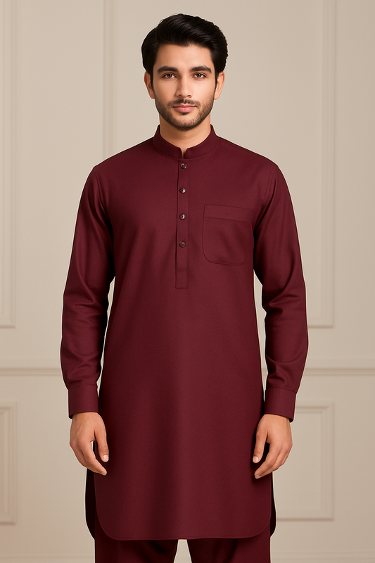 A young South Asian male model posing in a studio wearing a maroon wash and wear unstitched suit, showcasing traditional Pakistani menswear.